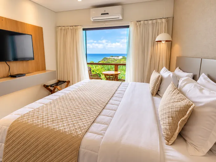 Cama e televisão do quarto duplo com janela para o mar